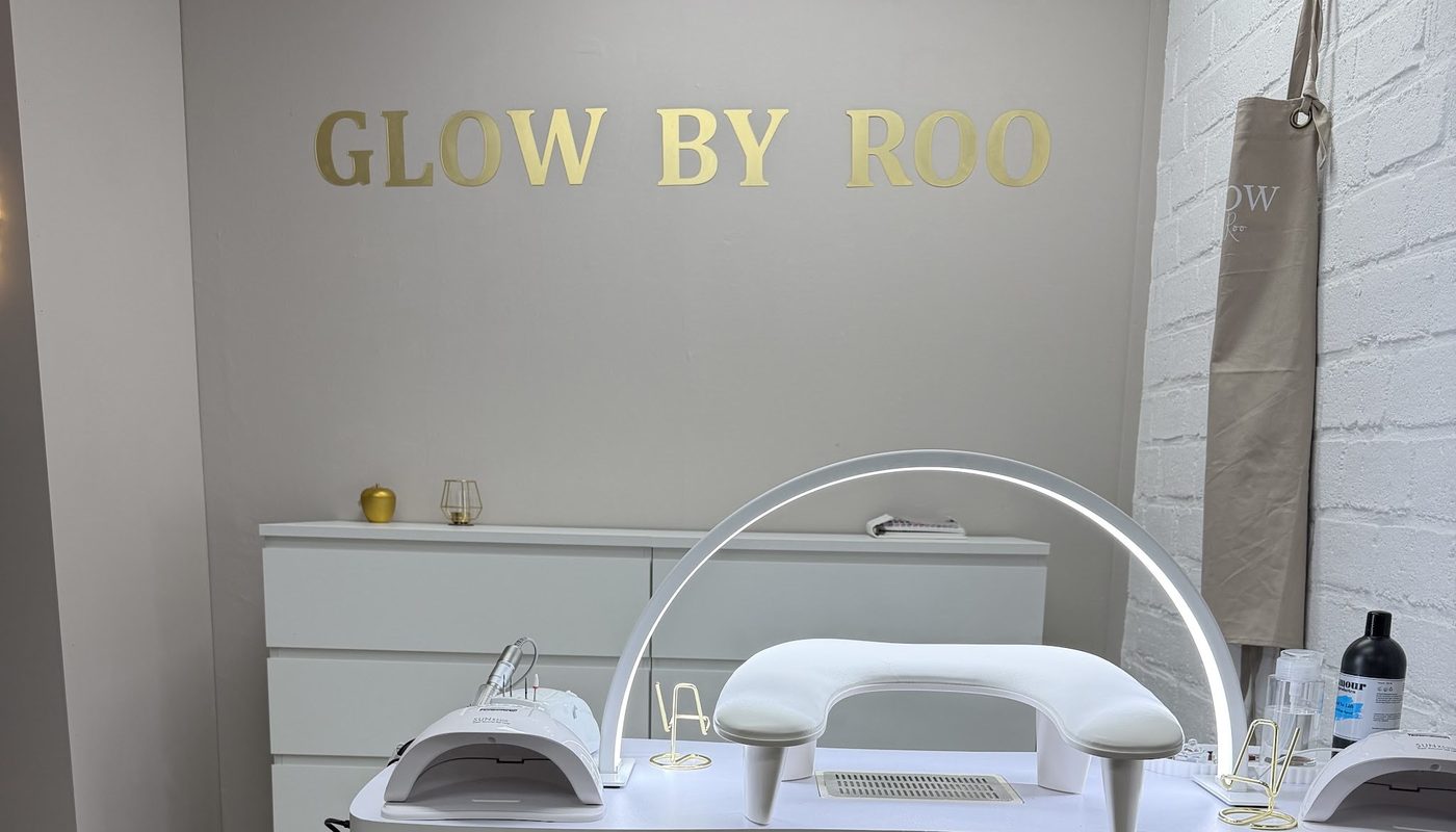 De salon: nageltafel met een witte ringlamp onder de gouden letters GLOW BY ROO op de muur